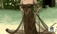 Met Gala 2024 gif. Closeup of the top of Emma Chamberlain's gothic-style Jean Paul Gaultier sleeveless black lace gown that features thin dark brown strands of lace weaved around her arms resembling brambles and ferns. She's wearing dark brown eye makeup and lipstick and a diamond collar necklace. 