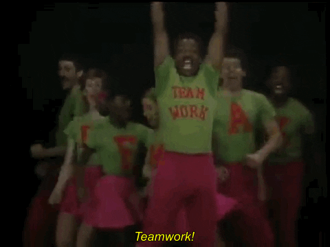 TV gif. On Reading Rainbow, LeVar Burton dances in unison with a group of kids wearing green shirts that spell out “Teamwork” as they all pull their fists down together and yell, “Teamwork!”