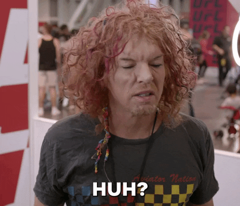 Celebrity gif. Carrot Top stares at us in confusion and looks around. His hair is curly and red and he says, "Huh?"