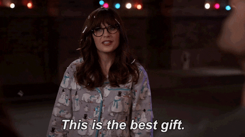 TV gif. Zooey Deschanel as Jessica Day from New Girl stands in snowman pajamas with white snippets of paper scattered throughout her hair. She gestures to the falling snow around her. Text, "This is the best gift."