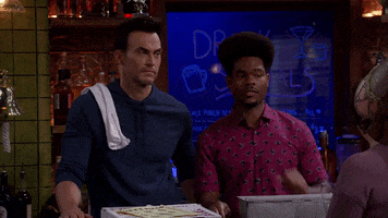 TV show gif. Cheyenne Jackson as Max and Julian Gant as Carter in Call Me Kat. They're standing behind a bar and they give each other a deadpanned high five.