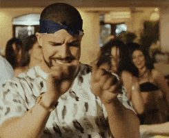 Music video gif. In a party scene from video for French Montana's "No Shopping," Drake dances, wincing and sticking out his tongue while gesturing like he's turning the wheel of a car.