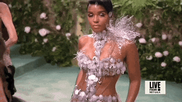 Met Gala 2024 gif. Slow motion clip of the top of Janelle Monae's dress showing a bursting silver poinsettia-like design at the top of one shoulder. Holographic disks dangle from her bustier.
