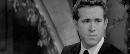 Celebrity gif. Ryan Reynolds is in black and white and he looks very distressed but suddenly turns towards the camera and gives us a cheeky stare down and smile.