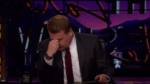 TV gif. James Cordon on The Late Late Show is sitting at his desk and has his hands on his face, pinching his eyes in annoyance.