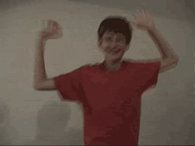 Video gif. Boy wearing red T-shirt and glasses smiles and dances with his elbows bent and his hands in the air.