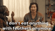 SNL gif. Simu Liu as a Thanksgiving dinner guest sits at a table holding silverware as he elaborates with his hands and says, "I don't eat anything with feathers anymore." Ego Nwodim as the dinner host cups a hand over her mouth in shock beside him.