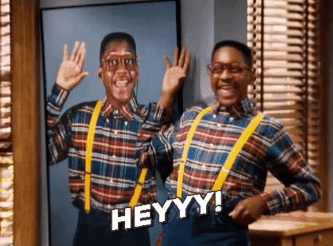 TV gif. Jaleel White as Steve Urkel from Family Matters stands next to a photo of himself waving and wearing an identical outfit with a red and blue plaid shirt, bright yellow suspenders, and high-waisted jeans. He mimics the photo by grinning and waving flirtatiously. Text reads, "Heyyy!"