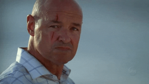 TV gif. Terry O'Quinn as John Locke in Lost opens his mouth to smile, revealing an orange in his mouth.