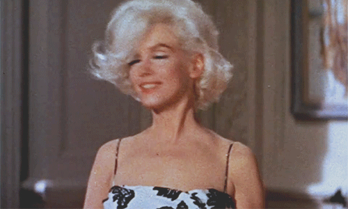 Celebrity gif. Marilyn Monroe gracefully flips her head of luscious blonde hair back while wearing a floral black and white, spaghetti strap dress.