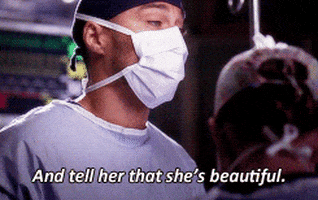 TV gif. Jesse Williams as Jackson Avery on Grey’s Anatomy wears surgical scrubs and a mask and looks over at someone, saying, “And tell her that she’s beautiful.”
