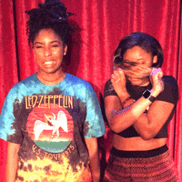 Celebrity gif. 2 Dope Queens' Jessica Williams cringing next to Phoebe Robinson, who pulls her hair to cover her face, as they stand in front of a red curtain.