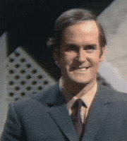 Celebrity gif. A young John Cleese smiles and raises his hand in the OK symbol. 