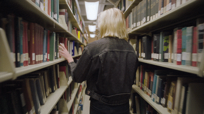 A woman is picking a book from the library shelf and walking forward.