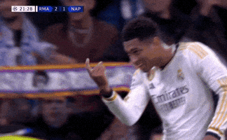 Sports gif. Jude Bellingham of Real Madrid smiles and uses an index finger to gesture to someone to coem closer as he walks on the field.
