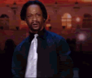 Celebrity gif. Wearing a black shirt with a white tie, Katt Williams looks around in confusion.