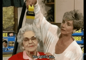 Video gif. Infomercial shows an old woman demonstrating an "as seen on TV" device that resembles a vacuum hose, on the white hair of an older woman who smiles placidly. Text reads, "You need this."