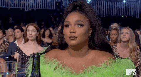 Celebrity gif. Lizzo at 2019 MTV Movie Awards shrugs and smiles coyly.