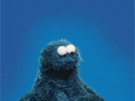 gif of Cookie Monster on a blue background, he picks up a red paper heart, looks at it, then points it towards you, smiling.