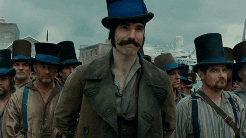 Movie gif. Daniel Day Lewis as Bill the Butcher in Gangs of New York stands menacingly in front of his top hat wearing street gang while they help remove his coat before battle. 