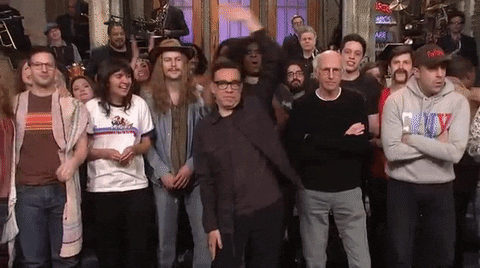 SNL gif. Fred Armisen in the center of the cast waves his arm over head while other cast members wave, except Larry David, whose arms are crossed.