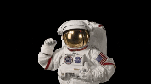 Video gif. An Astronaut in full gear, with the helmet shield down lifts his fist up into the air in celebration. 