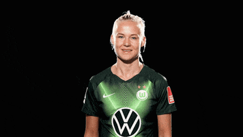 Sports gif. Professional footballer Pernille Harder smiles and points up with both hands like she wants you to check out her name.