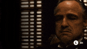 Movie gif. Marlon Brando as Vito Corleone in The Godfather scratches his chin, shakes his head and looks up, asking "who sent you?"