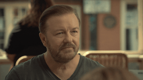 TV gif. Ricky Gervais as Tony Johnson in After Life sits across from a young boy in a restaurant. Tony stares up at a woman and then scrapes all the fish fingers off of the boy’s plate and stuffs them in his mouth, still keeping eye contact with the woman. The woman looks away in disgust as Tony chomps.