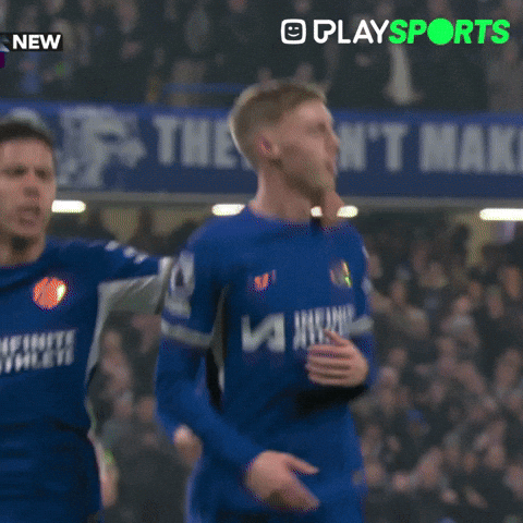 Sports gif. Cole Palmer from Chelsea Football Club is celebrating a goal and he puts his arms across his chest in an X. His teammate runs from behind and jumps on him.