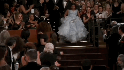 Oscars 2024 GIF. Porche Brinker of The Last Repair Shop lifts her gown to descend the stairs, surrounded by applause.

