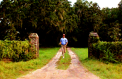Movie gif. Tom Hanks as Forrest Gump, in a red cap and a blue shirt, running furiously, turning from a dirt lane to a main road.