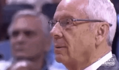 Sports gif. Roy Williams, head coach of UNC Tar Heels, exhales deeply and looks away in disappointment, shoulders drooping.