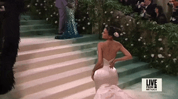 Met Gala 2024 gif. Slow motion close up of the back of Kylie Jenner's Oscar de la Renta gown that scoops down to a point at the mid back, hugging tight around her waist to reveal her waist to reveal the dramatic flare of her hips.