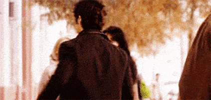 TV gif. Penn Badgley as Dan in Gossip Girl does a spin as he struts down the street and gives a random passerby a big high five, obviously in high spirits.