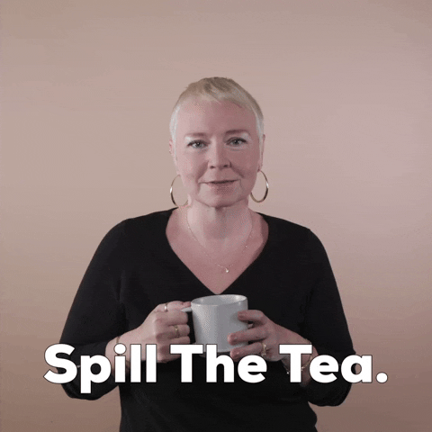 Reaction gif. A white woman with invisible disabilities, with hair styled in a sleek platinum pixie cut and big hoop earrings holds a mug and says demands "Spill the tea," punctuating the request with pursed lips and faux innocence.