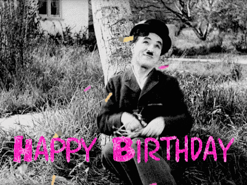 Movie gif. Black and white footage of Charlie Chaplin sitting on the grass against a tree tossing out his hands and bringing them back in with a shy or bashful expression. The video has been edited to make it look like he's throwing colorful confetti in the air. Text, "Happy Birthday."