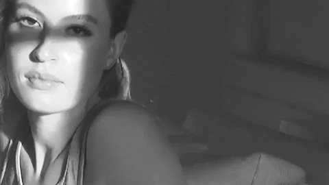 Music video gif. From Fletcher's video for "Sex With My Ex," black and white video zooms in on the face of a girl who looks to the side, seemingly annoyed, and then zooms in toward her breasts.