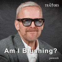 Sponsored gif. Traitors cast member Bob Harper smiles bashfully and then clutches his face with both hands. Text reads, “Am I blushing?”