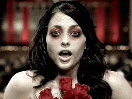 Music video gif. A woman from the music video "Helena" by My Chemical Romance. She holds a bouquet of roses and takes her last breath before she falls into a coffin, closing her eyes for good.