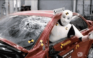 Video gif. A happy-looking crash test dummy hangs out of the driver's side window of a crashed car, pounding the door with his hand.