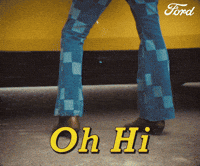 Sponsored gif. Camera pans up from the ground to a man leaning forward against a yellow vehicle. He suddenly whips his head around gives an intense look with one eyebrow raised. Text reads, “Oh hi.”