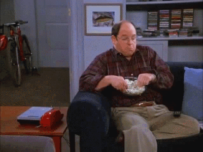 Seinfeld gif. Jason Alexander as George sits in an armchair in Jerry's apartment eating popcorn. He moves his head back and forth and looks thoughtfully down at the bowl.