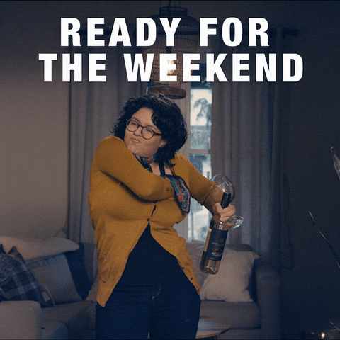 Video gif. A woman wearing office attire, reaches down her shirt and pulls her bra out, holding a wine bottle and glass in the other hand. She twirls the bra over her head with a huge smile on her face. Text, "Ready for the weekend."