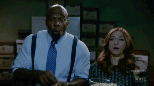 Tv gif. Terry Crews as Terry Jeffords and Chelsea Peretti as Gina Linetti on Brooklyn Nine Nine move side to side as they dance together. Terry and Gina gasp in surprise as they watch something and laugh. Gina holds a bowl of popcorn as she dances.