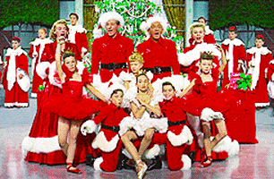 Movie gif. Dressed in red and white like the Clauses, Bing Crosby, Danny Kaye, Rosemary Clooney, and Vera Ellen as Bob, Phil, Betty, and Judy in White Christmas sing together while standing behind children posed onstage.