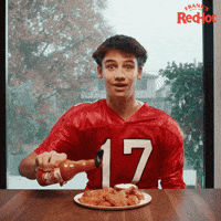 Sponsored gif. Smiling teenage boy in a red football jersey shakes Frank’s RedHot sauce onto a plate of chicken wings. He’s suddenly surrounded by cheering fans, a tiger mascot, and a coach as confetti rains down around them. Text reads, “Touchdown.”