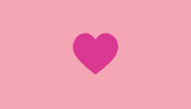 Illustrated gif. Hot pink heart against a pale pink background expands and contracts while small white, yellow, and red fireworks explode in the foreground.