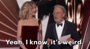 Nodding his head and spreading his hands, Billy Crystal says “Yeah, I know, it’s weird.” Meg Ryan stands next to him, first watching him and then smiling.