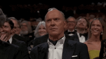 Oscars 2024 GIF. Michael Keaton, seated at the Oscars, dramatically sneers and gestures to bring it.